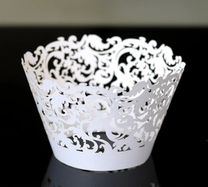 Intricate laser-cut white lace cupcake wrapper with Baroque hollow pattern on black surface