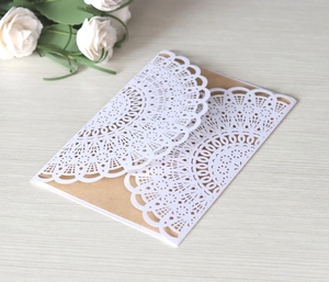 Detail of vintage kraft paper wedding invitation with white laser-cut lace and rose
