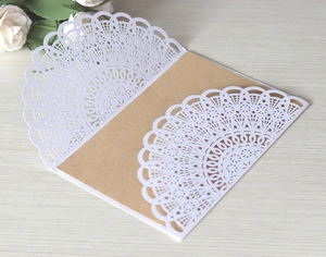 Detailed laser-cut white lace invitation pocket with intricate mandala pattern on wood