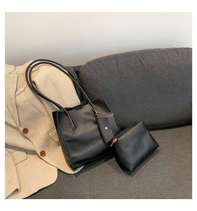Three-piece set of black pebble leather tote bags on grey fabric sofa background