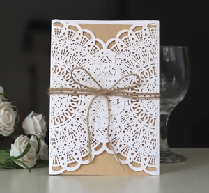 Close-up of laser-cut lace wedding invitation with kraft paper and rustic twine bow