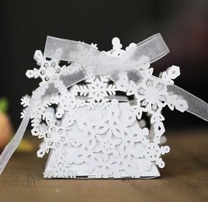 Close-up of laser-cut snowflake candy box with white organza ribbon on wood