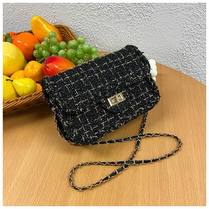Detail of tweed crossbody bag featuring metallic lock and gold chain strap on table