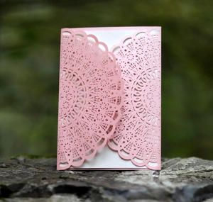 Detailed laser-cut pink pearlescent paper wedding invitation on a natural stone background