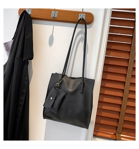 Detailed view of black pebbled faux leather tote bag with matching envelope pouch hung at home