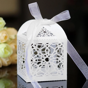 Detail of white laser-cut wedding candy box with geometric hollow patterns and ribbon