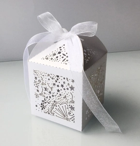 Macro shot of laser-cut white wedding favor box with star patterns and a chiffon ribbon bow