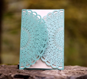 Close-up of laser-cut light blue wedding invitation with pearlescent mandala pattern