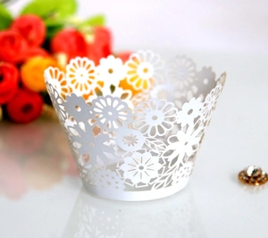 Macro detail of laser-cut white cupcake wrappers with elegant daisy and leaf patterns