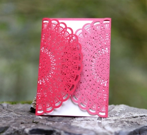 Close-up of red laser-cut invitation card with mandala pattern on forest rock