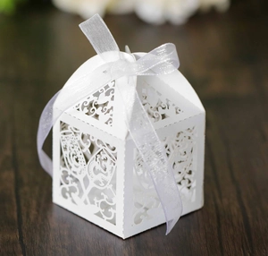 Close-up of laser-cut white wedding favor box with heart patterns and white ribbon bow