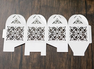 Flat lay of laser-cut white wedding favor box template on a textured wood background
