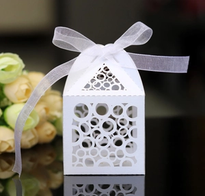 Macro detail of laser-cut house shaped gift box with white ribbon on reflective surface