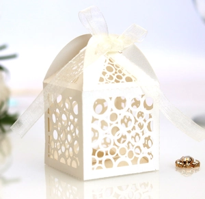 Close-up of cream white laser-cut favor box with intricate patterns and satin ribbon