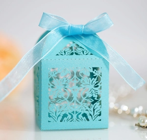 Macro detail of laser-cut floral patterns on light blue wedding candy favor box with ribbon