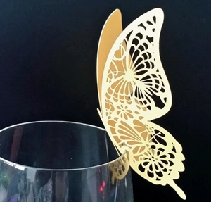 Golden 3D laser-cut butterfly decoration card placed on a glass edge with black background
