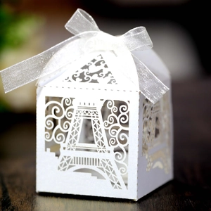 Laser-cut Eiffel Tower favor box with white ribbon on dark wood texture background