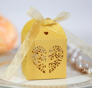 Macro shot of laser-cut gold wedding favor box with heart tree pattern and organza ribbon