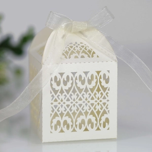 Close-up of laser-cut wedding favor box with white ribbon and ornate floral patterns