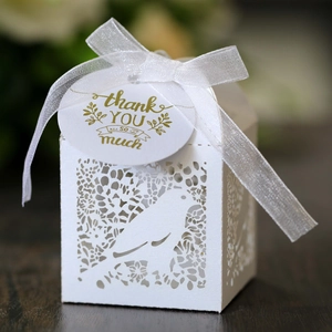 Detail of laser-cut white favor box with bird patterns, ribbon and thank you tag