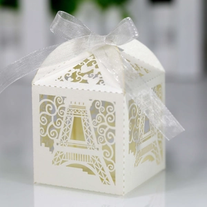 Detail of laser-cut Eiffel Tower candy box with elegant cream hollow patterns and silk ribbon