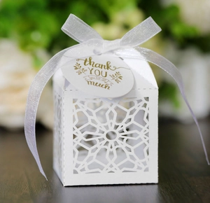 Detail of white laser-cut wedding favor box with star patterns, ribbon and thank you card