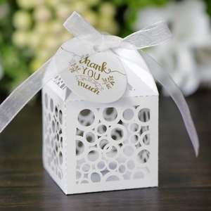 Laser-cut white wedding favor box with round patterns, satin ribbon, and thank you tag