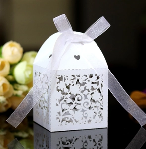 Close-up of white laser-cut floral wedding candy box with ribbon bow and heart detail