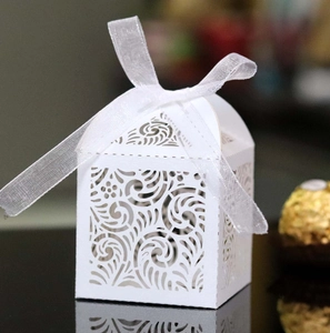 Macro view of white laser-cut wedding favor box with elegant floral patterns and ribbon