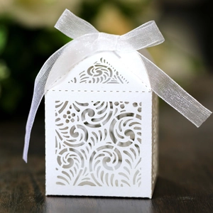 Macro shot of laser-cut scroll patterns on a white wedding favor box with organza ribbon