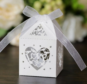 Macro shot of laser-cut white wedding favor box with LOVE lettering and ribbon