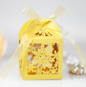 Macro shot of yellow laser-cut snowflake paper gift box with a matching ribbon tie