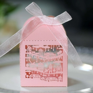 Detail of pink laser-cut wedding favor box with European architecture and white silk ribbon