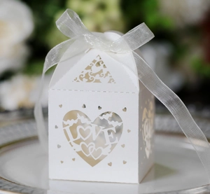 Macro detail of laser-cut white heart favor box with LOVE motif and organza ribbon
