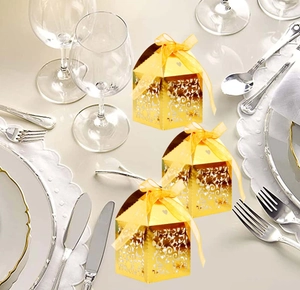 Detail of gold laser-cut hollow candy boxes with silk ribbons on elegant dinner table