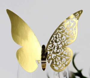 Detail of laser-cut gold butterfly card with intricate hollow vine patterns on wine glass