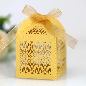 Detail of laser-cut gold wedding favor box with floral patterns and a matching ribbon bow