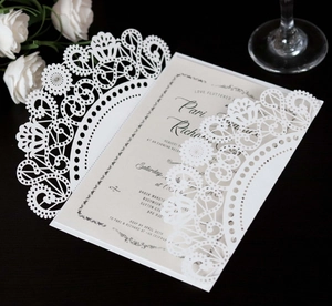 Close-up of laser-cut wedding invitation with intricate lace pattern and elegant printing