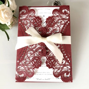 Detailed laser cut burgundy wedding invitation with floral patterns and a cream satin bow