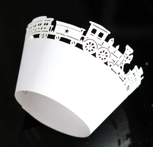 Detail of laser-cut white cupcake wrapper featuring a delicate train pattern design
