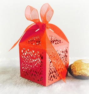 Detail of red laser-cut candy box with heart pattern and orange organza ribbon bow