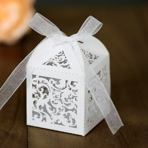 White laser-cut wedding favor box with hollow scroll patterns and organza ribbon bow