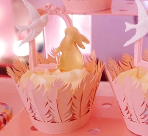 Intricate laser-cut cake wrappers in light pink with elegant feather pattern and bird toppers