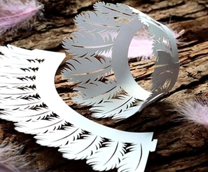 Intricate laser-cut white feather cupcake wrappers for elegant wedding cake decoration