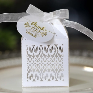 Macro shot of laser-cut white wedding favor box with delicate ribbon and thank you card