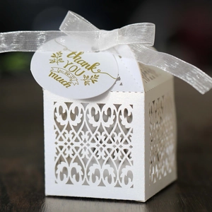 Close-up of laser-cut gift box with white ribbon and thank you tag on wooden background