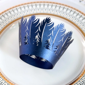 Dark blue laser cut cupcake wrapper with feather crown pattern on a white porcelain plate