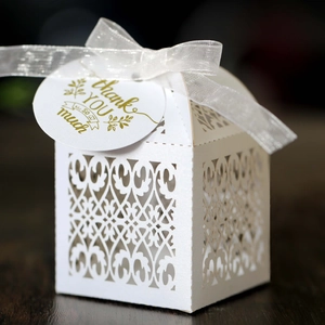 Close-up of laser-cut white favor box with thank you tag and white ribbon on dark wood