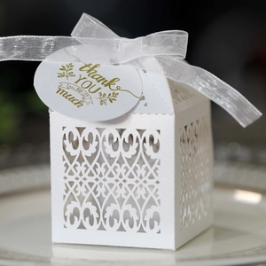 Close-up of laser-cut white favor box with silk ribbon and gold thank you gift tag