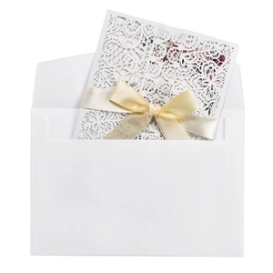 Close-up of laser-cut invitation card with a cream silk ribbon bow and matching envelope